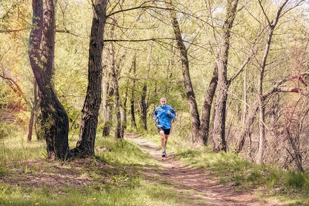 在一个温暖的春日里，一位身着黑色和蓝色衣服的老人在森林里跑步。