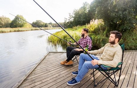 休闲与人的概念-男性朋友在湖边钓鱼和喝啤酒。男性朋友在湖上钓鱼和喝啤酒