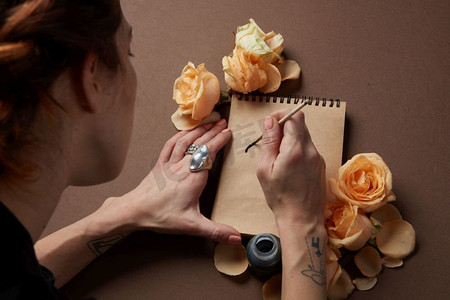 手写浪漫情书摄影照片_妇女与画笔写在纸与玫瑰花蕾。手用画笔写情书