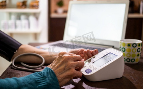 虚拟的摄影照片_远程医疗概念老年妇女在厨房测血压的视频在线咨询中