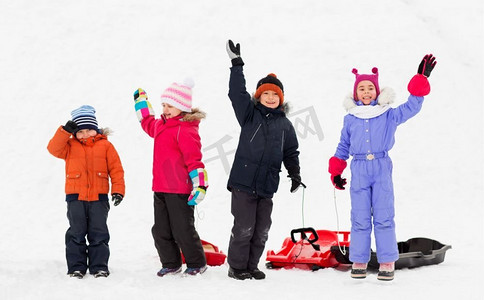 一群小孩子摄影照片_童年，雪橇和季节概念—一群快乐的小孩子与雪橇在冬天挥舞着手。快乐的孩子与雪橇挥舞的手在冬天