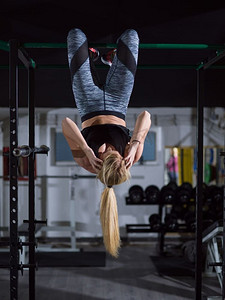 在交叉健身房做腹肌练习的女运动员倒挂在单杠上。正在做腹肌锻炼的女性