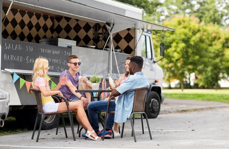 休闲和人的概念—快乐的朋友与饮料坐在餐桌上的食品卡车。朋友喝饮料坐在餐桌在食品卡车