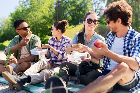 休闲与人的概念-一群快乐的朋友在夏季公园野餐和吃三明治。朋友们在夏令营野餐快乐