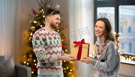 人和假日概念—在丑毛衣党的快乐夫妇的肖像与圣诞礼物。快乐的夫妇在圣诞毛衣与礼品盒
