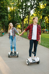 一对年轻的情侣在公园的陀螺板上骑车。带电动旋转板的户外娱乐设施。平衡运输技术