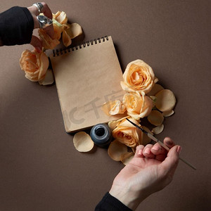 信纸摄影照片_女性的手写下来在信纸与花在棕色桌子上，顶视图。音符和花朵