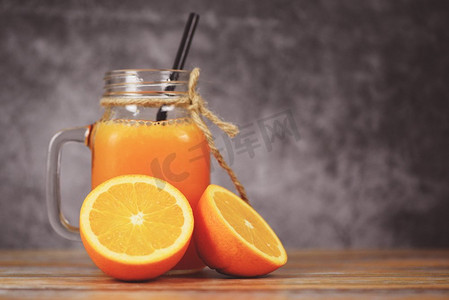 新鲜水果片摄影照片_橙汁在玻璃罐和新鲜的橘子水果片在木桌/静物玻璃汁在黑暗背景