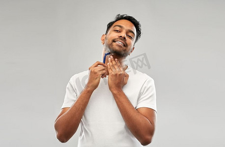 修饰和人概念—年轻的印度人刮胡子与手动剃刀刀片在灰色背景印度男子刮胡子与剃刀刀片