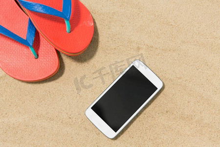 技术，假期和暑假概念—智能手机和人字拖在沙滩上。智能手机和人字拖在沙滩上
