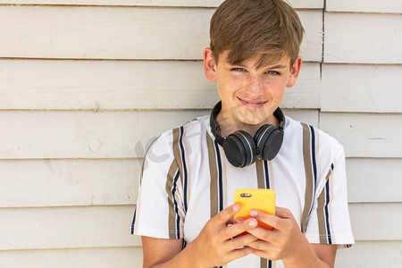 男孩青少年青少年男孩外面使用他的移动手机和蓝牙无线耳机为社会媒体