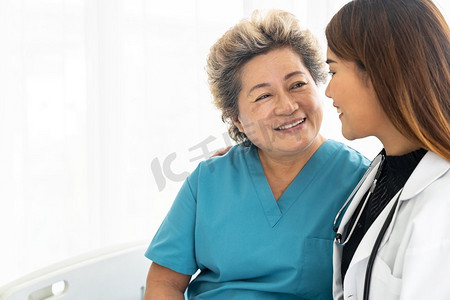 身着制服的年轻女医生在医院病房探视老年妇女患者时拥抱并微笑着