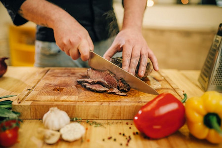 男厨师手用刀切烤肉片，顶视图。男人准备蔬菜牛肉。厨师在锅与烤肉和蔬菜