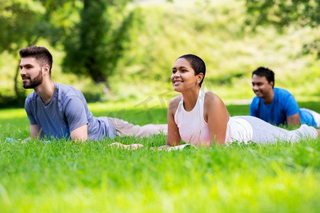 健身，运动和健康的生活方式概念—一组快乐的人做瑜伽斯芬克斯姿势在夏季公园。一群人在夏季公园做瑜伽