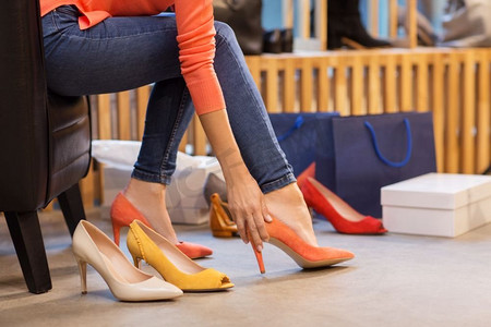 销售，购物，时尚和人的概念—年轻的妇女选择高跟鞋在商店。年轻女子尝试高跟鞋在商店