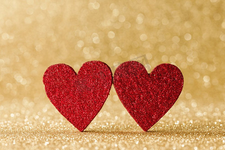 金色金光摄影照片_两个小手工制作的红色闪光心脏在明亮的金光bokeh背景情人节卡。两颗心在散景背景