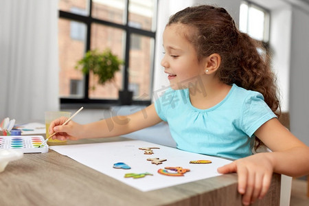 童年，爱好和休闲概念—小女孩用画笔画木纸板项目在家里。小女孩在家里画木制物品