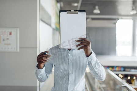 乌木商人用一本笔记本覆盖了他的脸在商场。成功的商人，穿着正式服装的黑人，购物中心 
