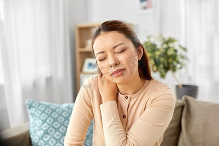 人，健康和问题概念—疲惫的亚洲妇女在家里遭受颈部疼痛。亚洲妇女遭受疼痛在脖子在家里