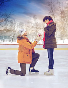建议，浪漫和爱的概念—愉快的夫妇与订婚戒指在户外溜冰场。男子与戒指作出建议在溜冰场