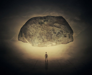 超现实主义的图像是一个男人，背着一个袋子，站在一条雾蒙蒙的街道下面的一块巨大的挤压岩石。生活压力和压力概念。