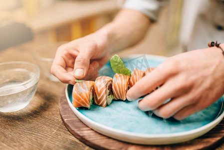 日本厨房摄影照片_男性烹饪寿司卷与鲑鱼在木桌，日本食品准备过程。日本料理寿司卷