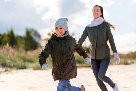 家庭，休闲和人的概念—快乐的母亲和小女儿沿着秋天的海滩跑步。快乐的家庭运行沿着秋天海滩