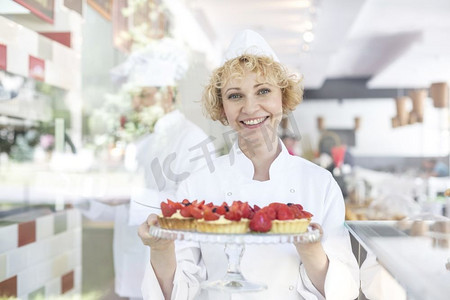 微笑的成熟厨师的肖像持有新鲜草莓馅饼在托盘在餐厅