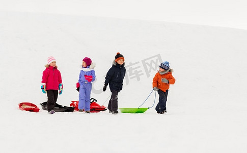 小孩子摄影照片_童年，雪橇和季节概念—一群快乐的小孩子在冬天雪橇。快乐的小孩子与雪橇在冬天