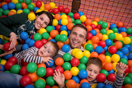 快乐的家庭享受自由时光年轻的父母和孩子在儿童游戏室的游泳池里玩五颜六色的球