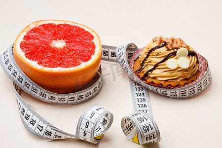 选择的概念：健康的低热量或不健康的高热量食物，减肥或增肥。葡萄柚和蛋糕纸杯蛋糕与卷尺