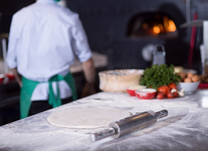 撒面粉摄影照片_厨师准备面团为比萨饼滚动与手撒面粉表。厨师准备披萨面团