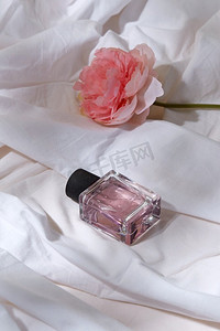 床单褶皱摄影照片_美丽，香水和对象概念—瓶香水和花在白色床单与折叠。一瓶香水和花在白色床单