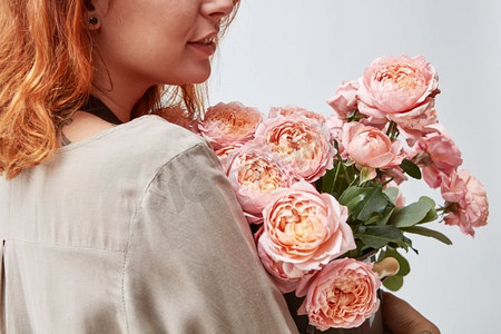 情人玫瑰摄影照片_美丽的年轻女孩与一束粉红色玫瑰在花瓶。母亲节妇女拿着一个花瓶与新鲜的粉红色玫瑰