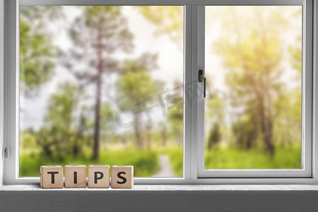 TIPS标志在窗户上，可以看到阳光下有高大树木的绿色花园