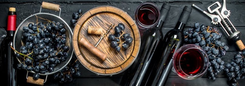 葡萄酒背景。加葡萄的红酒和一个陈旧的桶。在黑色的乡村背景上..葡萄酒背景。加葡萄的红酒和一个陈旧的桶。
