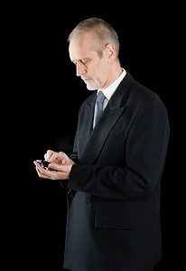 黑色背景高级摄影照片_高级商人在黑色西装写短信或拨号码在他的移动电话，在黑色背景
