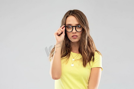 人物概念-穿着黄色T恤、戴着眼镜的年轻女子或十几岁的女孩，背景是灰色。戴眼镜的年轻女子或少女