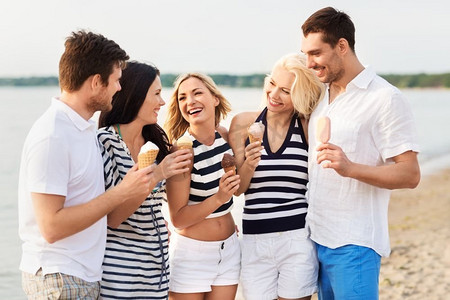 友谊、休闲和人的概念-一群穿着条纹衣服在海滩上吃冰淇淋的快乐朋友。快乐的朋友在海滩上吃冰淇淋