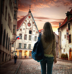 女孩旅行者背着背包站在塔林的背景中。欧洲城市的老街。