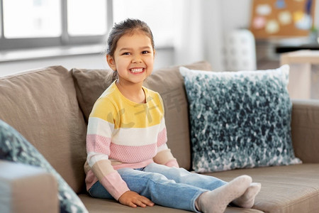 人与童年的概念--快乐微笑的小女孩坐在家里的沙发上。开心的笑着的小女孩坐在家里的沙发上