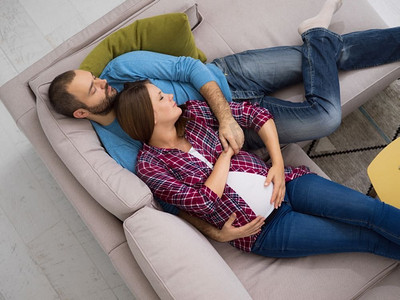 怀孕的夫妇在沙发上放松。幸福的怀孕夫妇在家中的沙发上放松的俯瞰