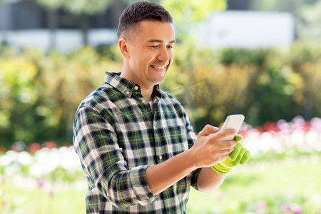 园艺和人的概念—中年男子与智能手机在夏季花园。快乐的人与智能手机在夏季花园