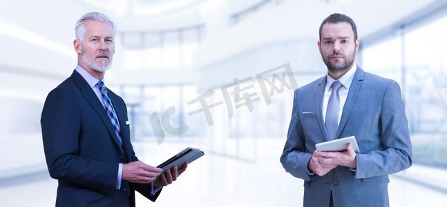 两个商人的肖像。在现代IT公司前面使用平板电脑的两个同事商人的肖像