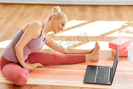 健身、科技和健康生活方式理念--在瑜伽馆里用笔记本电脑锻炼的女性。拿着笔记本电脑在瑜伽室锻炼的女子
