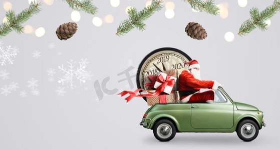 圣诞节到了摄影照片_圣诞节倒计时到了。汽车上的圣诞老人在送新年礼物和灰色背景的时钟。汽车上的圣诞老人倒计时