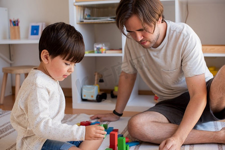 小孩子玩玩具摄影照片_小孩子和他的父亲在家里玩木积木。在家上学。呆在家里家庭时间