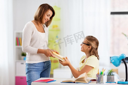 教育，家庭和学习的概念—快乐的母亲给女儿的书在家里。快乐的母亲给女儿书在家里