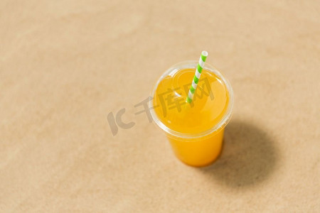 饮料，假期和暑假概念—一杯橙汁与稻草在海滩沙滩上。一杯橙汁与稻草在沙滩上