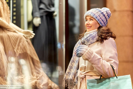 节日和人们的概念快乐女人拿着购物袋在冬城的橱窗里看着。冬天提着购物袋的快乐女人